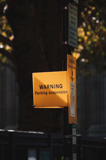 A rectangular sign with a black background and raised gold lettering displaying 'NO PARKING' is mounted on a light green wooden wall comprised of vertical panels. The sign appears to be made of metal, with visible mounting brackets on each side. The wall may be part of a residential or commercial building in a parking-restricted area. The image is taken during daylight, with even lighting highlighting the texture of the wooden panels and the sign's details. This visual context supports the understanding of parking restrictions, which can be relevant for house removals and furniture transport when navigating tight or restricted access points in W2, Paddington. Removal Companies Paddington may encounter such signage during the home relocation process, especially when coordinating parking or delivery access for moving services.